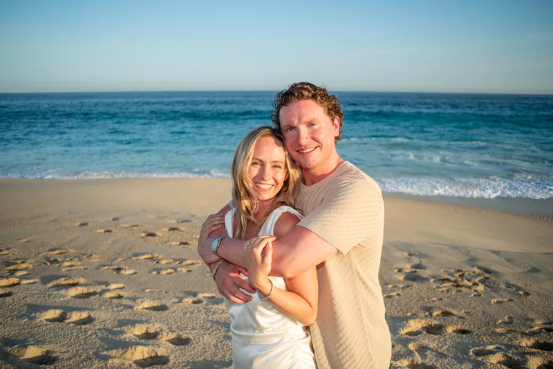 Jacquelyn and Jake embracing on the beach in Los Cabos, both smiling at the camera
